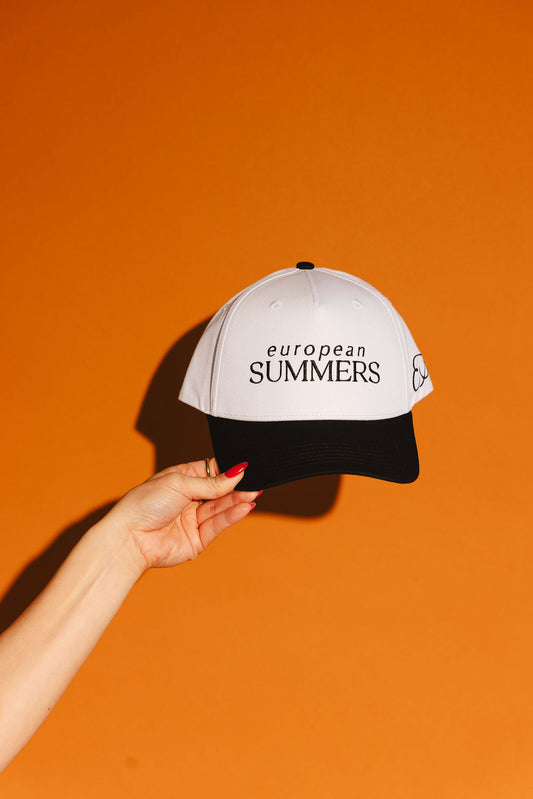 Hand holding a cap with 'European Summers' text against an orange background