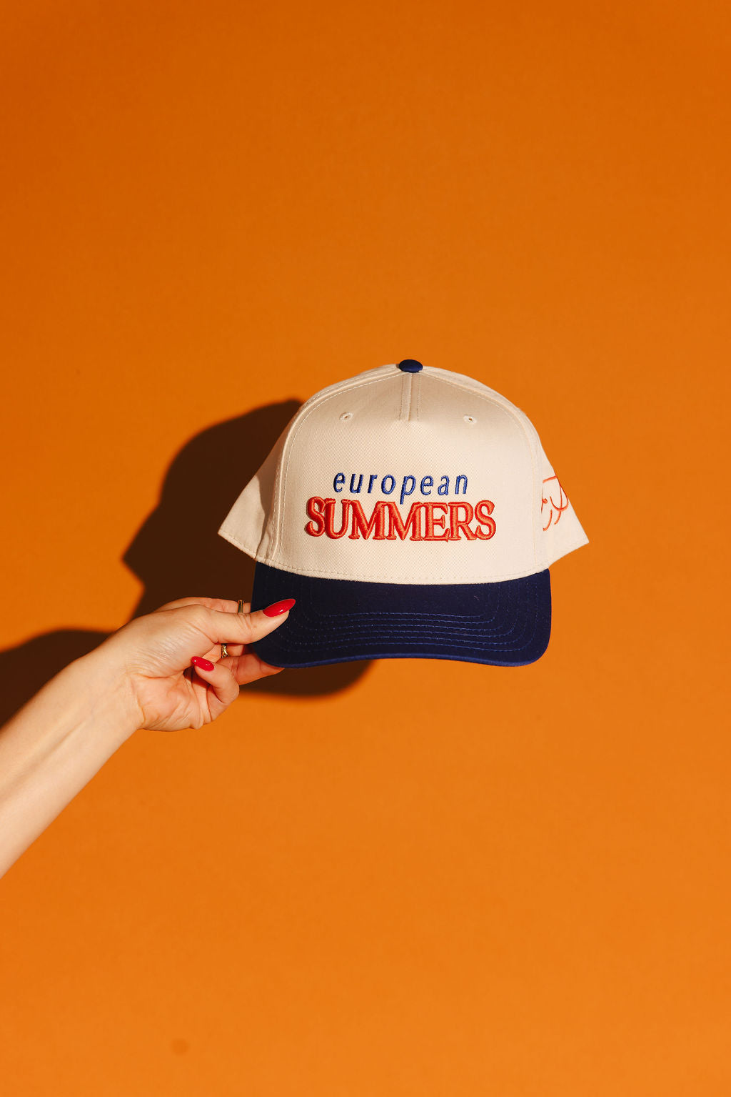 Cap with 'European Summers' text held by a hand against an orange background
