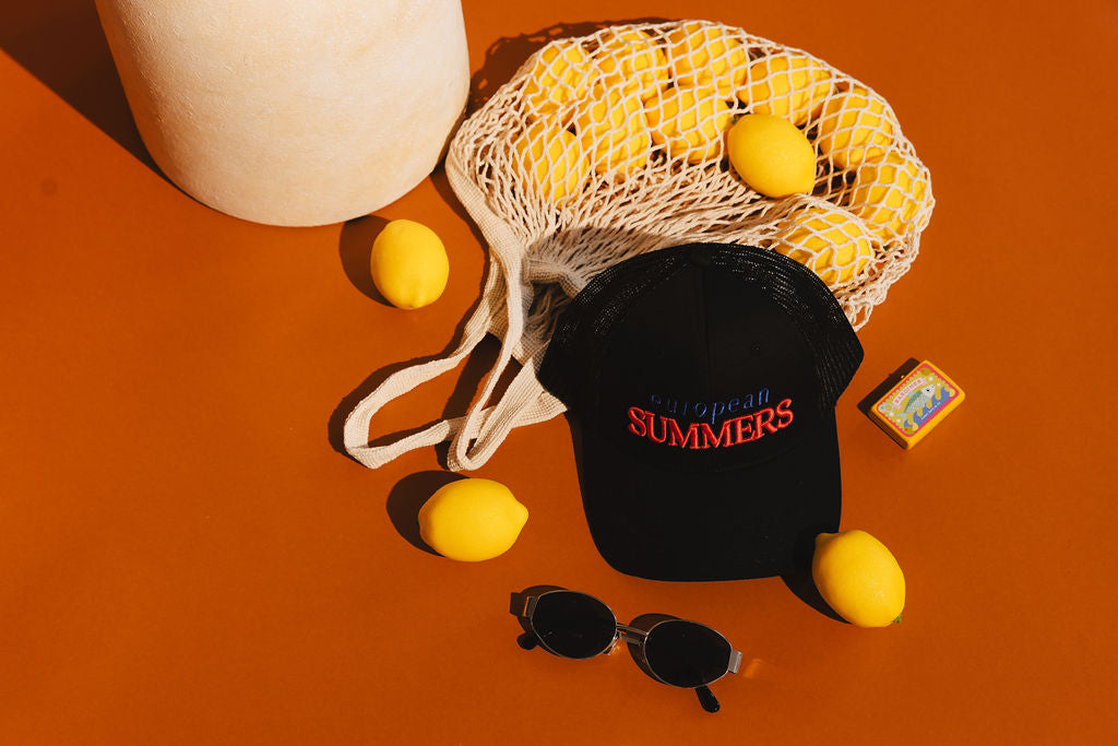 Black cap with 'Superb Summers' text, sunglasses, and lemons on an orange background