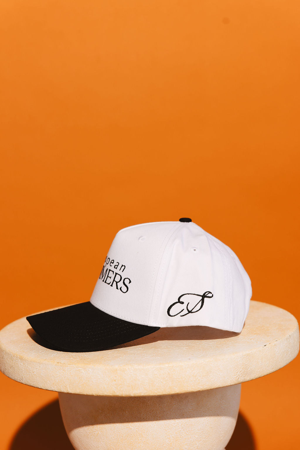 White cap with black visor and branding on an orange background