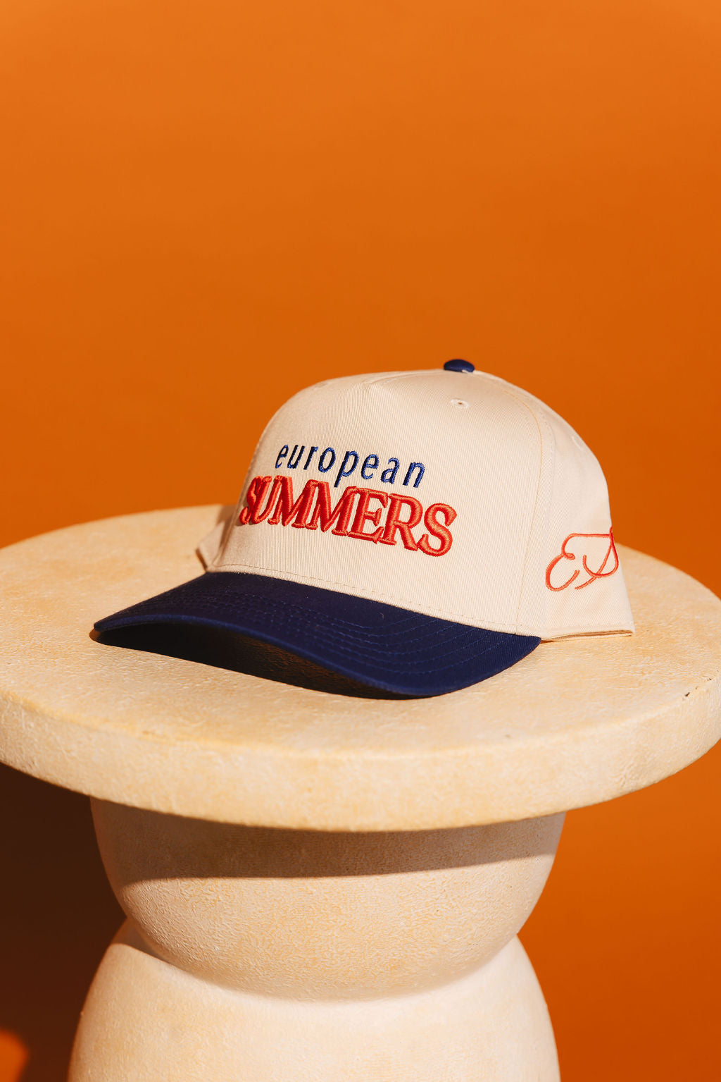 Cap with 'European Summers' text on a wooden stand against an orange background