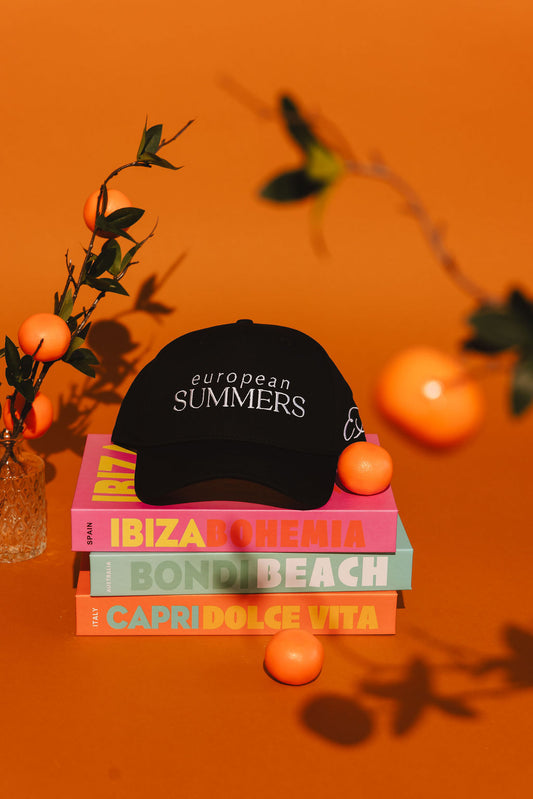 Black cap with 'European Summers' text on a stack of books with orange background